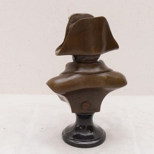 May include: Bronze bust sculpture of a man wearing a bicorne hat on a black marble base. The bust is signed "F. Barrias" and numbered "2313".