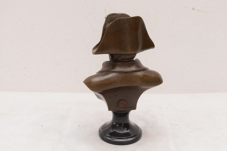 May include: Bronze bust sculpture of a man wearing a bicorne hat on a black marble base. The bust is signed "F. Barrias" and numbered "2313".