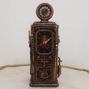 May include: A bronze-colored decorative clock shaped like a vintage fuel pump. It features a circular gauge at the top, a central clock face with Roman numerals, and intricate copper-toned piping and mechanical details across the rectangular body.