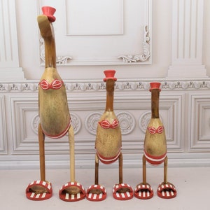 Peut inclure: Trois figurines de canard en bois avec des chapeaux rouges et des maillots de bain à rayures rouges et blanches. Les canards sont debout sur des sandales à rayures rouges et blanches.