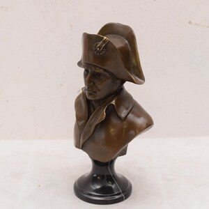 May include: Bronze bust sculpture of a man wearing a bicorne hat. The bust is on a black marble base.