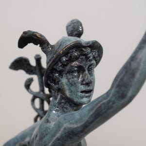 May include: A bronze statue of a figure with a hat and raised arm. The statue has a weathered, verdigris finish, with details like a winged staff and a hat with a gold trim. The sculpture is a classical art piece.