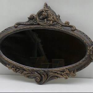 May include: An oval-shaped wall mirror with an ornate, gold-painted, metal frame. The frame features intricate floral and scroll designs.