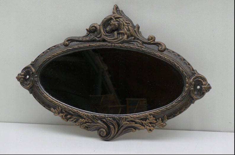 May include: An oval-shaped wall mirror with an ornate, gold-painted, metal frame. The frame features intricate floral and scroll designs.