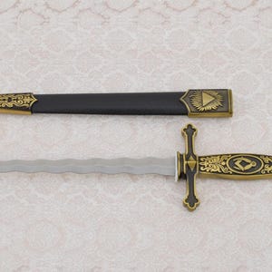 May include: A decorative dagger with a black handle and a silver blade. The handle is adorned with gold accents and intricate designs. The blade is double-edged and has a wavy pattern.