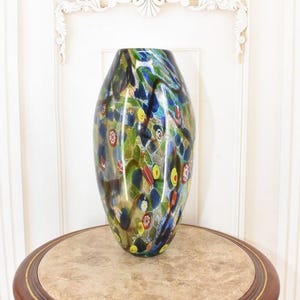 May include: A large, colorful glass vase with a bulbous shape. The vase features a swirling pattern of blue, green, yellow, and red colors. It sits on a round, marble-topped table with a dark wood base.