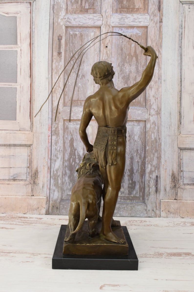 May include: Bronze sculpture of a man holding a whip and standing next to a lion. The sculpture is on a black base.