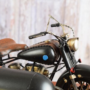 May include: A detailed model motorcycle with a sidecar. The motorcycle features a black body, brown leather seat and fuel tank accents. The sidecar is also black with brown leather details. The model has a vintage, antique aesthetic.