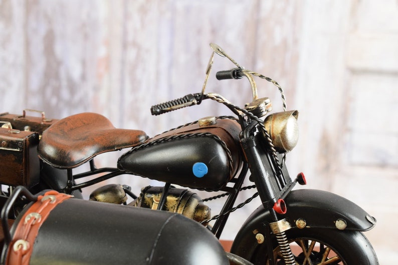 May include: A detailed model motorcycle with a sidecar. The motorcycle features a black body, brown leather seat and fuel tank accents. The sidecar is also black with brown leather details. The model has a vintage, antique aesthetic.