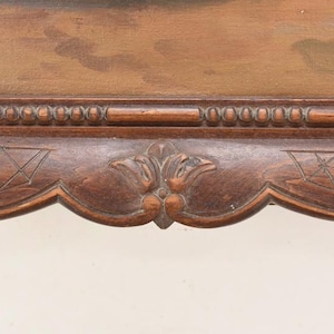 Pu&ograve; includere: Primo piano di una sezione di una cornice in legno marrone scuro. La cornice presenta intagli intricati, tra cui una fila di piccoli dettagli arrotondati sul bordo superiore. La parte inferiore presenta un motivo floreale decorativo.