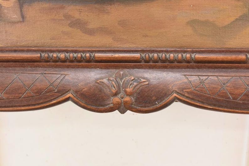Pu&ograve; includere: Primo piano di una sezione di una cornice in legno marrone scuro. La cornice presenta intagli intricati, tra cui una fila di piccoli dettagli arrotondati sul bordo superiore. La parte inferiore presenta un motivo floreale decorativo.