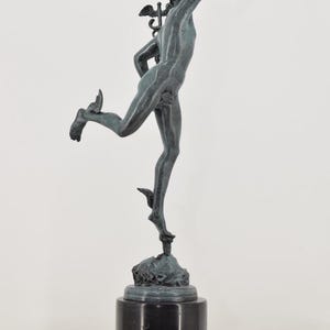 May include: A bronze sculpture of a male figure in motion, with wings on his head and feet, atop a black marble base. The figure is reaching upwards with one arm, capturing a sense of movement and grace.