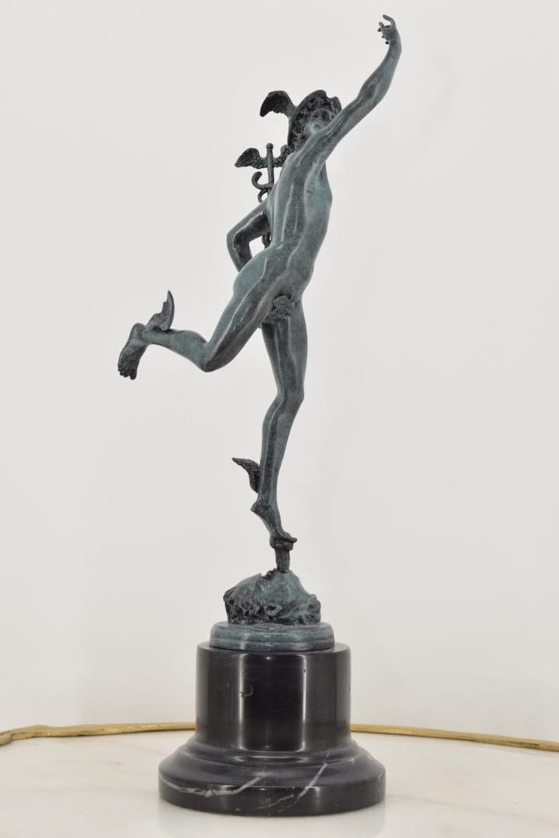 May include: A bronze sculpture of a male figure in motion, with wings on his head and feet, atop a black marble base. The figure is reaching upwards with one arm, capturing a sense of movement and grace.