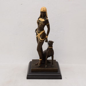 May include: Bronze sculpture of a woman in a gold headdress and a gold-accented outfit, standing with a black panther on a black base.