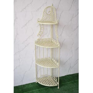 May include: Off-white metal corner shelf with four tiers. The shelves are semi-circular with a decorative, openwork design. The top shelf has a decorative, arched top. The shelf is freestanding and suitable for indoor or outdoor use.
