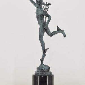 May include: A bronze statue of a figure in motion, possibly Mercury, with a winged helmet and staff. The statue is mounted on a black marble base. The figure is depicted with one arm raised and one leg extended, suggesting movement.