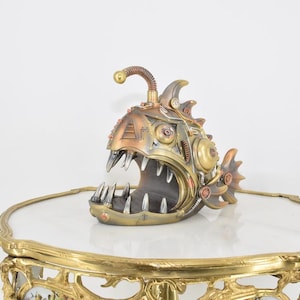 May include: A steampunk-style anglerfish sculpture with a detailed, intricate design. The sculpture is made of metal and has a bronze, copper, and silver finish.