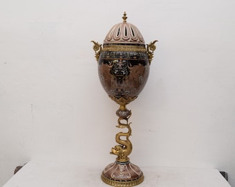 May include: A large, ornate, gold and brown ceramic vase with a lid and a dragon-shaped base. The vase is decorated with intricate floral and geometric patterns.