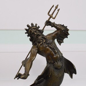 Puede incluir: Una escultura de bronce de una criatura marina m&iacute;tica, posiblemente Poseid&oacute;n o Neptuno, sosteniendo un tridente. La figura tiene una corona, pelo largo y una cola de pez. La escultura es detallada y parece antigua.