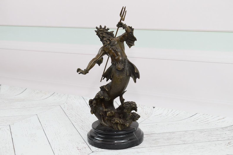 Puede incluir: Estatua de bronce de una criatura marina m&iacute;tica, posiblemente Poseid&oacute;n o Neptuno, sosteniendo un tridente. La escultura presenta intrincados detalles de la cara, la corona y la cola de pez de la figura. La estatua est&aacute; montada sobre una base de m&aacute;rmol negro.