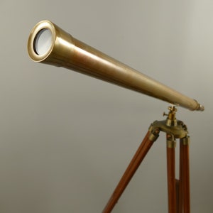 May include: A brass telescope mounted on a wooden tripod. The telescope has a long, cylindrical barrel and a lens at the end. The tripod has three wooden legs and brass hardware. The overall design is vintage.