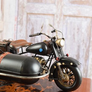 May include: A detailed black motorcycle with a sidecar, featuring brown leather seats and luggage. The model has gold-colored accents on the wheels, headlight, and other parts. A blue circle is on the gas tank.