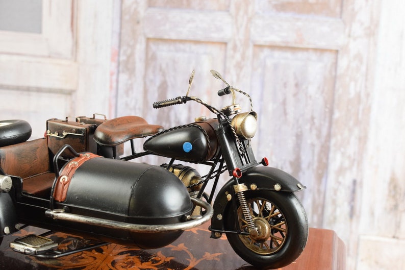 May include: A detailed black motorcycle with a sidecar, featuring brown leather seats and luggage. The model has gold-colored accents on the wheels, headlight, and other parts. A blue circle is on the gas tank.