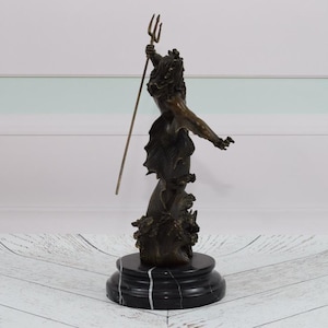 Puede incluir: Escultura de bronce de una figura sosteniendo un tridente, montada sobre una base de m&aacute;rmol negro. La figura tiene una apariencia detallada y texturizada, con ropas fluidas y una corona. La escultura se encuentra sobre un fondo blanco y celeste.