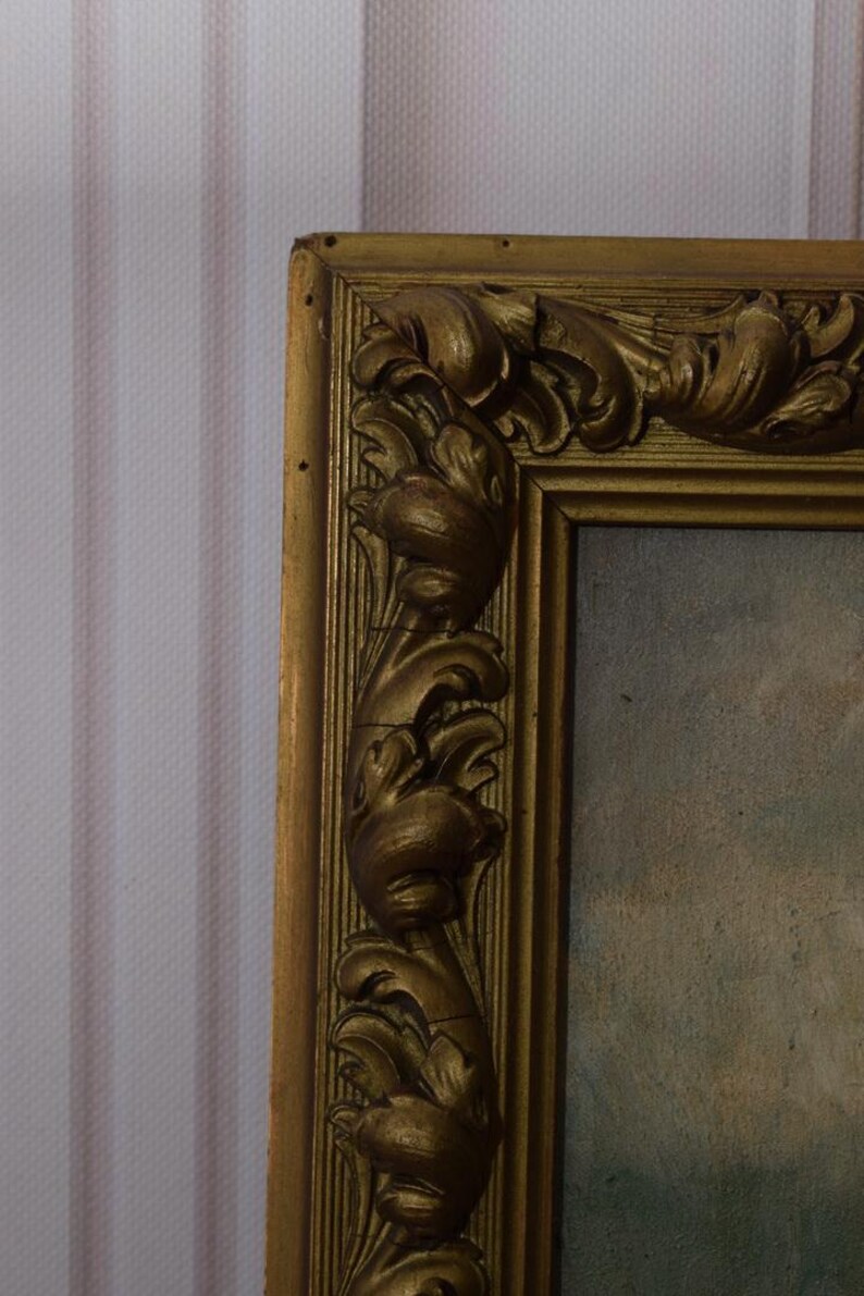K&ouml;nnte beinhalten: Ein verzierter Bilderrahmen in Gold mit einem detaillierten, geschnitzten Design. Der Rahmen ist aus Holz und hat eine leicht abgenutzte Oberfl&auml;che.