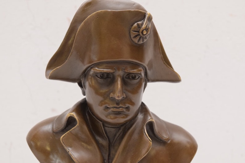 May include: Bronze bust sculpture of a man wearing a bicorne hat. The sculpture is detailed and realistic, capturing the man's facial features and the texture of his clothing.