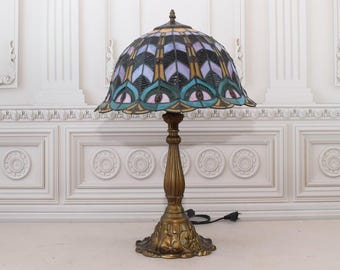 May include: A stained glass table lamp with a gold base and a colorful, geometric design. The lampshade features shades of blue, green, purple, and gold.