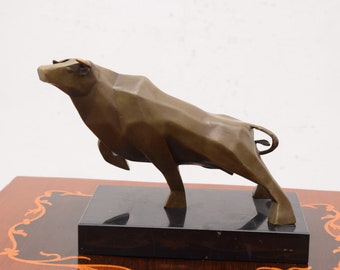 Puede incluir: Una escultura de bronce de un toro de pie sobre una base de mármol negro. El toro está estilizado con formas geométricas y tiene la cabeza levantada.