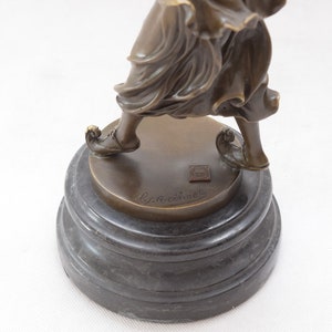 Op de afbeelding: Bronzen beeldje van een vrouw in een vloeiende jurk, staande op een zwarte marmeren voet. Het beeldje is gesigneerd "Lyraccini" op de voet.