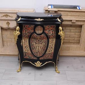 Può includere: Un mobile nero con dettagli dorati e motivi ornati. Il mobile presenta una finitura nera lucida, finiture dorate e intricati disegni rossi e dorati sul davanti. Anche le gambe e le maniglie sono dorate. Un mobile decorativo.