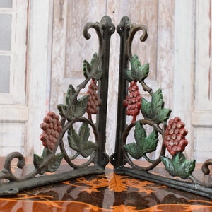 May include: A pair of cast iron shelf brackets with a grapevine design. The brackets are painted in shades of green, red, and black.