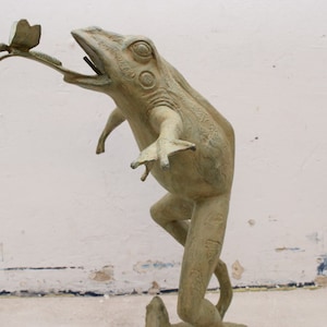 May include: A green frog statue with a detailed texture, leaping up to catch a butterfly with its mouth open.