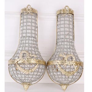 May include: Two ornate wall sconces. Each has a clear, crystal-like body within a silver grid, topped with a gold-coloured crown. Gold-coloured decorative elements adorn the base and midsection, creating an elegant, vintage aesthetic. A pair of decorative wall lights.