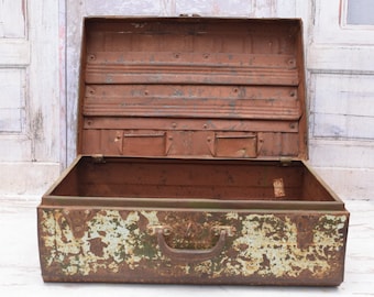 Puede incluir: Una maleta de metal vintage con una pátina verde y marrón. La maleta está abierta y el interior está vacío. La maleta tiene un asa en la parte superior.
