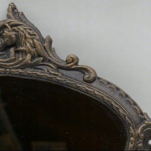 May include: A decorative oval mirror with a dark brown frame. The frame is ornate and features a detailed design with a gold finish.