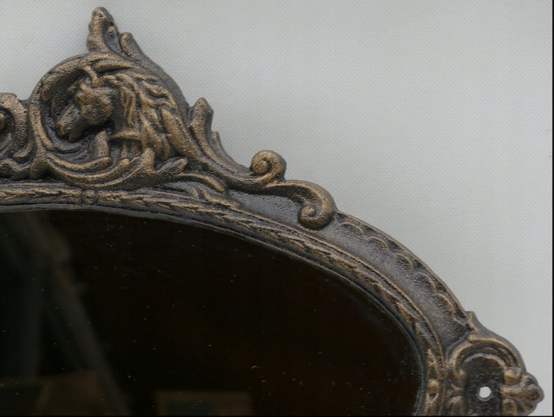 May include: A decorative oval mirror with a dark brown frame. The frame is ornate and features a detailed design with a gold finish.