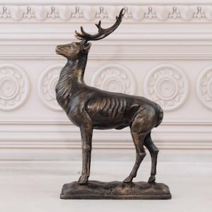 Może przedstawiać: Brązowa statuetka jelenia z porożem, stojąca na prostokątnej podstawie. Jeleń jest zwrócony w prawo i ma szczegółowy, realistyczny design.