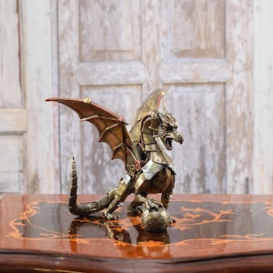 Może przedstawiać: Rzeźba smoka w stylu steampunk, w odcieniach brązu i mosiądzu. Smok ma ruchome skrzydła, szczegółową głowę i elementy mechaniczne. Jest umieszczony na dekoracyjnej powierzchni, ukazując misterne rzemiosło.