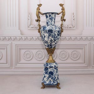 May include: A large, blue and white porcelain vase with gold accents and a decorative base. The vase is decorated with a floral pattern and features two gold figures on the handles.