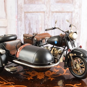 May include: A detailed black and brown motorcycle with a sidecar. The motorcycle features a brown leather seat, a small suitcase, and a spare tire on the sidecar. The wheels have a gold finish, and the headlights are a bright gold color.