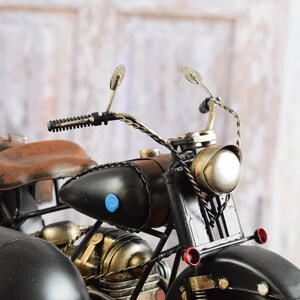 May include: A detailed model of a vintage motorcycle with a sidecar. The motorcycle features a black body, brown seat, and luggage. The headlight and other details are metallic. The sidecar is black and has a rounded shape.