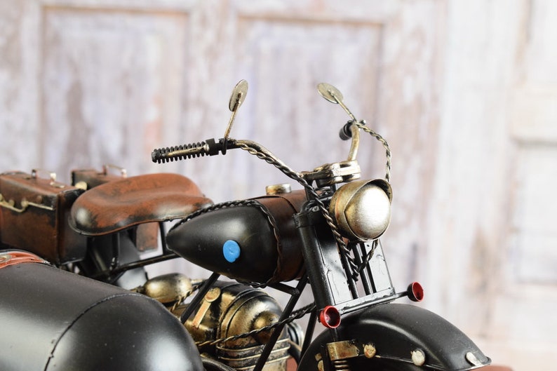 May include: A detailed model of a vintage motorcycle with a sidecar. The motorcycle features a black body, brown seat, and luggage. The headlight and other details are metallic. The sidecar is black and has a rounded shape.