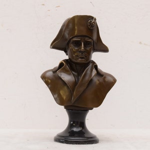 May include: Bronze bust sculpture of Napoleon Bonaparte wearing a bicorne hat on a black pedestal.