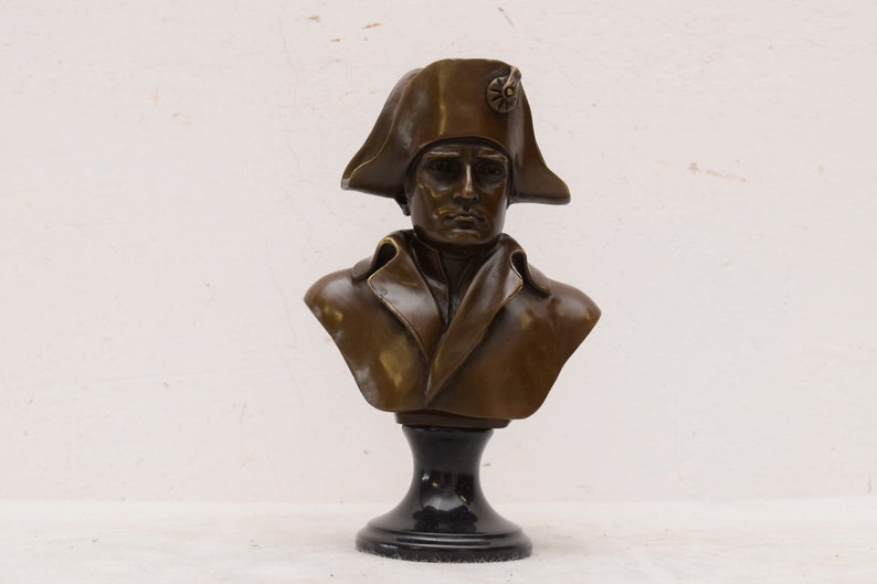May include: Bronze bust sculpture of Napoleon Bonaparte wearing a bicorne hat on a black pedestal.