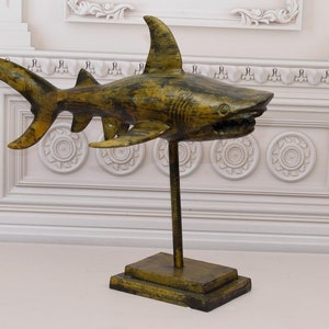 May include: A wooden shark sculpture with a distressed green finish, mounted on a wooden stand. The shark has a detailed mouth and fins.