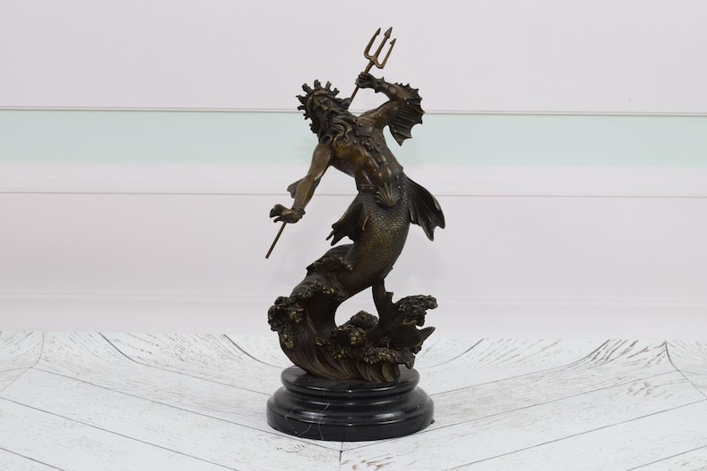 Puede incluir: Estatua de bronce de una criatura marina m&iacute;tica, posiblemente Poseid&oacute;n o Neptuno, con un tridente. La figura tiene una corona, cola de pez y est&aacute; montada sobre una base de m&aacute;rmol negro. La estatua es de color bronce oscuro.